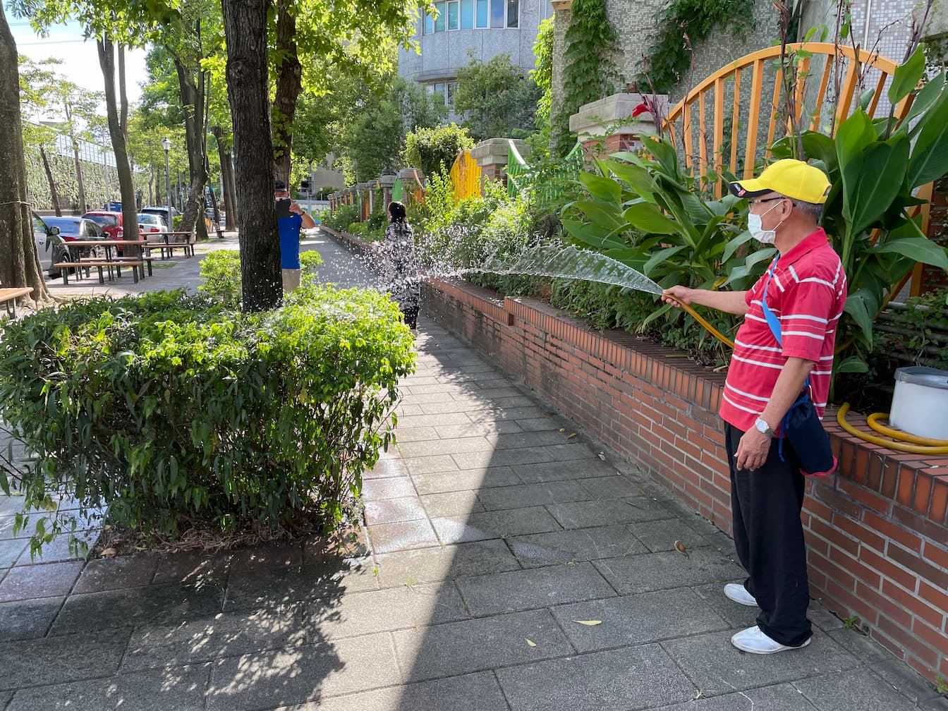 湯大哥看著里長示範雨撲滿的儲水效果，也拿起雨撲滿接出的水管澆灌花圃（Source: 劉學墉攝）