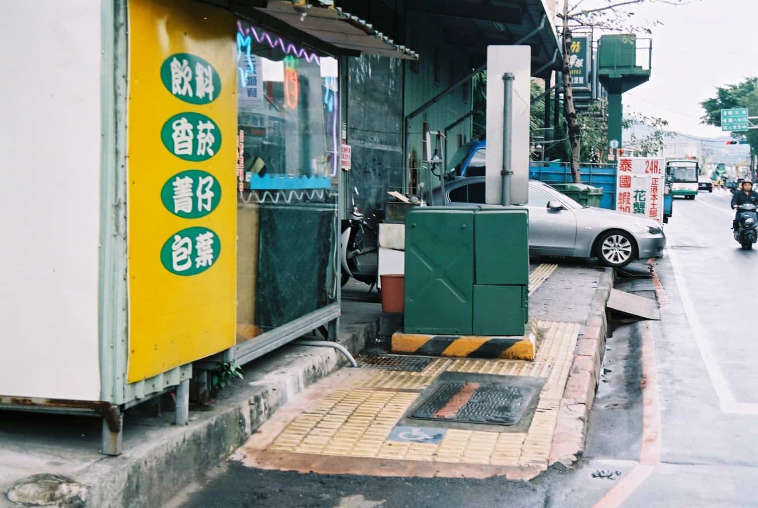變電箱大剌剌地置放在人行道中央，後方店家的招牌以及汽車的停放，都讓行動不便者在城市中的移動顯得十分掙扎（Source: sunboy／CC BY-NC-ND 2.0）